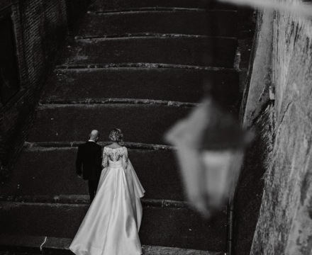 Sposa Il Giardino Fiorito delle Spose in abito con coda lunga mentre sale le scale con lo sposo durante il matrimonio