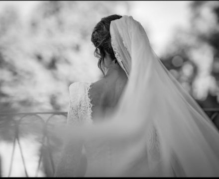 Sposa Il Giardino Fiorito delle Spose con abito in pizzo e velo lungo mentre si affaccia durante il matrimonio