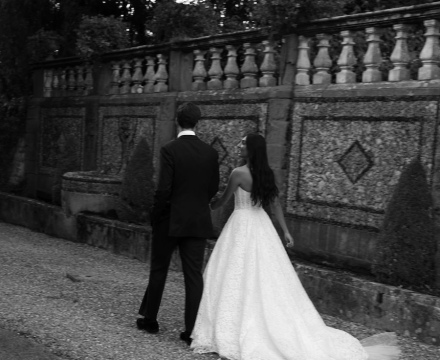Sposa Il Giardino Fiorito delle Spose con abito da sposa in pizzo e velo lungo mentre cammina con lo sposo durante il matrimonio all’aperto