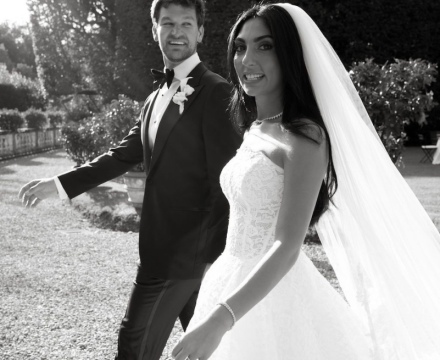 Sposa Il Giardino Fiorito delle Spose con abito da sposa in pizzo e velo lungo mentre cammina con lo sposo durante il matrimonio all’aperto
