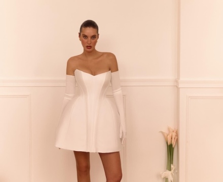 Abito da sposa corto in stile moderno con corpetto strutturato, scollatura omerale e guanti lunghi, presso Il Giardino Fiorito delle Spose a Roma.