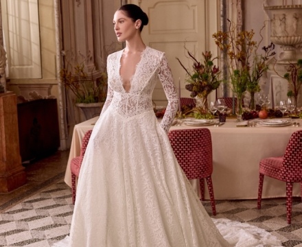 Abito da sposa principesco interamente in pizzo, con maniche lunghe e profonda scollatura, presso Il Giardino Fiorito delle Spose a Roma.